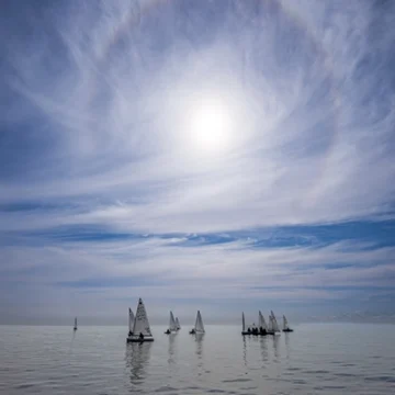 Cielo con halo solar sobre el mar, con varias embarcaciones de vela navegando en aguas tranquilas, en una imagen capturada en la costa de Torrevieja