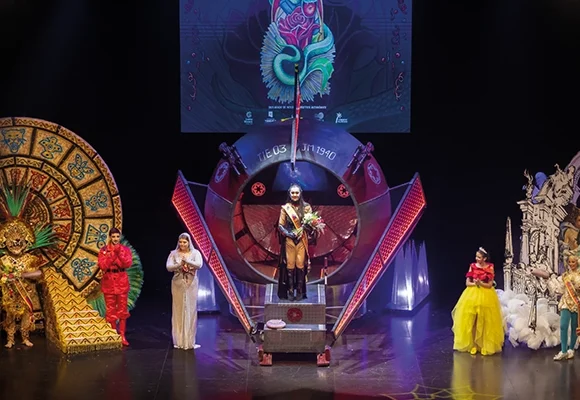 Escenario del Teatro Municipal de Torrevieja durante la gala de coronación del Carnaval, con los nuevos reyes y reinas ataviados con espectaculares trajes temáticos. Decorado con estructuras representativas de diversas culturas y elementos de fantasía, el evento destaca por su grandiosa puesta en escena