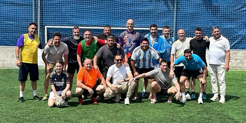 va3410-amigos-gloriet1 alt="Participantes del encuentro entre Amigos de la Ermita y Amigos de la Glorieta posan junto a sus hijos en el campo de fútbol 5 de césped artificial de MC Los Ángeles."