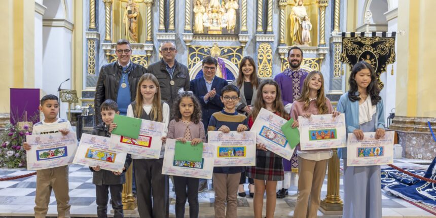 Niños y niñas premiados posando con sus dibujos y diplomas en el altar de la iglesia junto a los organizadores