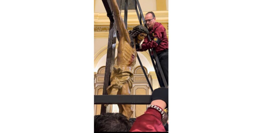 Un costalero subido a una escalera asegurando la imagen del Cristo durante la ceremonia de bajada