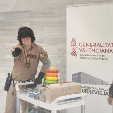 Tres miembros de Ghostbusters España caracterizados con sus trajes y equipos junto a un carro lleno de juguetes en el Hospital de Torrevieja