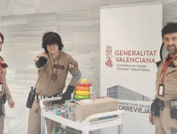 Tres miembros de Ghostbusters España caracterizados con sus trajes y equipos junto a un carro lleno de juguetes en el Hospital de Torrevieja