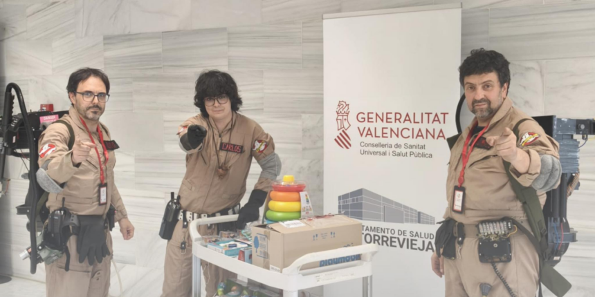 Tres miembros de Ghostbusters España caracterizados con sus trajes y equipos junto a un carro lleno de juguetes en el Hospital de Torrevieja