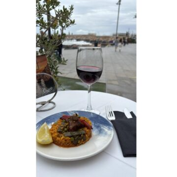 Ración de arroz con carne y verduras acompañada de una copa de vino tinto en una terraza