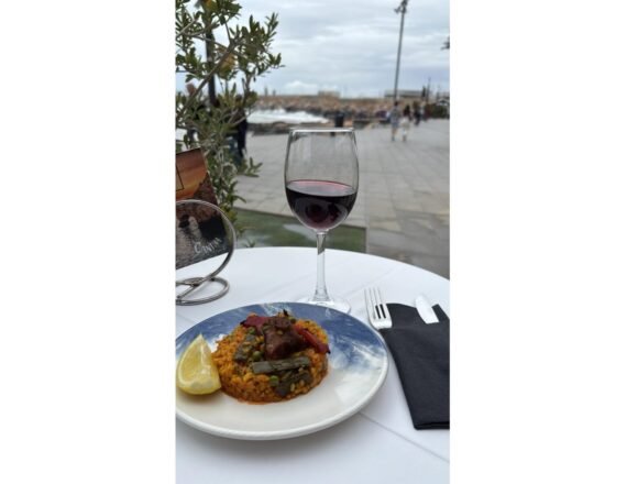 Ración de arroz con carne y verduras acompañada de una copa de vino tinto en una terraza