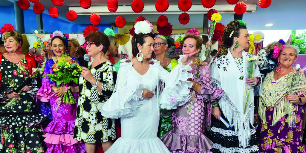 Participantes de distintas generaciones lucen trajes de flamenca en el desfile intergeneracional organizado como antesala a la Feria de Mayo