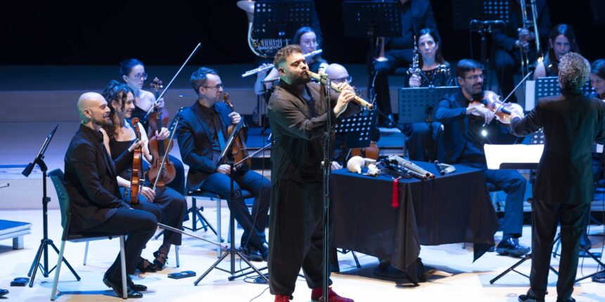 Abraham Cupeiro interpreta una melodía con un instrumento ancestral durante su espectáculo "PANGEA" en el Auditorio Internacional de Torrevieja, acompañado por una sección de orquesta