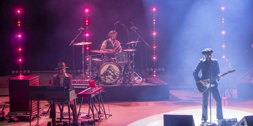 El vocalista de Sidecars cantando y tocando la guitarra en primer plano durante el concierto, acompañado por el teclista y el batería