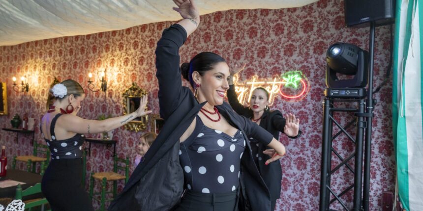 Varias mujeres con trajes de flamenca de lunares bailan en el interior de una de las casetas decoradas de la Feria de Mayo