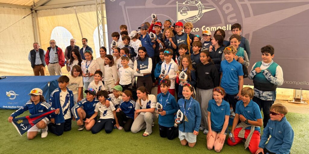 Grupo de jóvenes regatistas de la clase Optimist B celebrando con trofeos durante la entrega de premios en Campello
